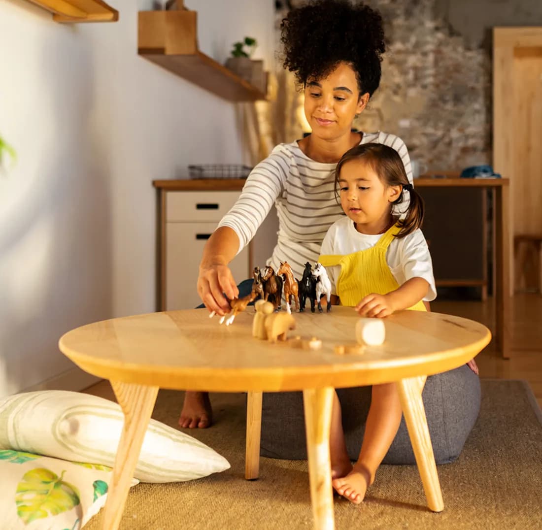 Parent and child playing with toy horses at a low wooden table